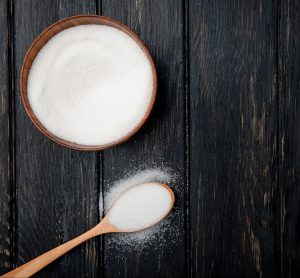 top view white granulated sugar wooden bowl wooden spoon black rustic background with copy space scaled e1668599799158
